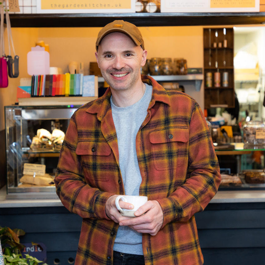 man in plaid shirt and cap standing in from of a cafe counter