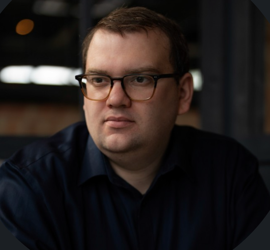 Man wearing glasses and a dark shirt against a blurred background